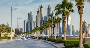 A cityscape with modern skyscrapers, palm trees lining the street, and a clear sky. - Piks Key - Grandeur Residences (Dubai)