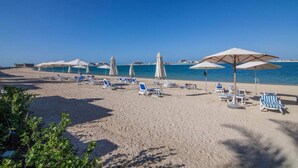 A beach with sun loungers and umbrellas, a clear sky, and a calm sea. - Piks Key - Grandeur Residences (Dubai)