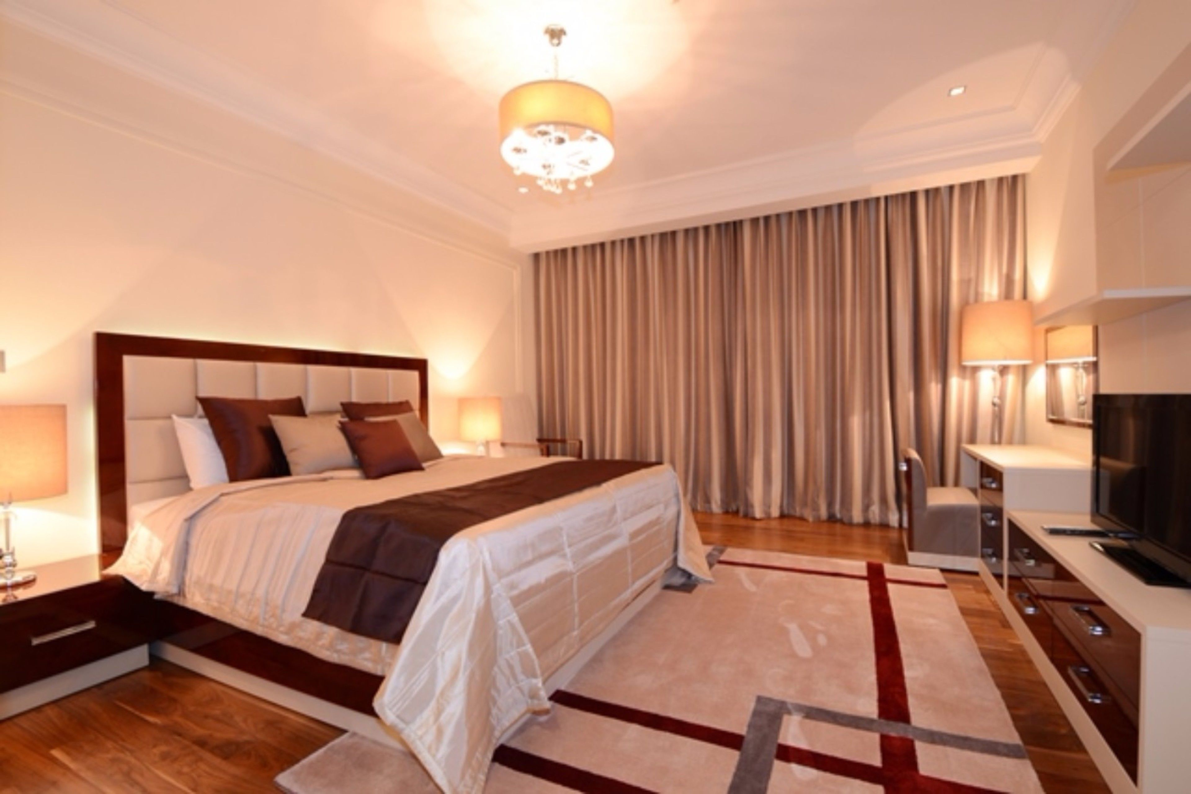A modern hotel room with a large bed, a TV, a desk, and a lamp.