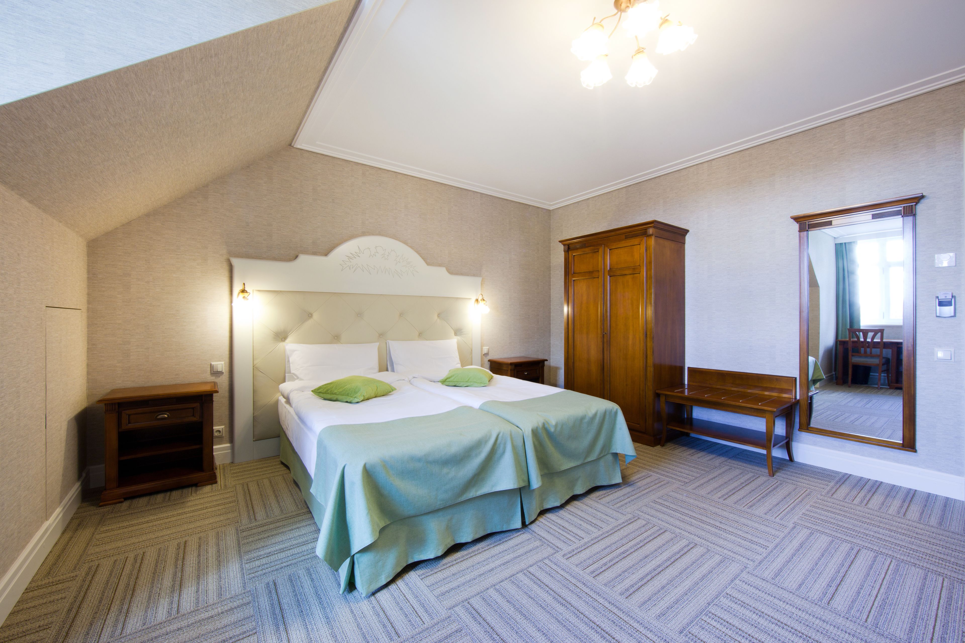 A bedroom with a large bed, a nightstand, a wooden wardrobe, and a bench.