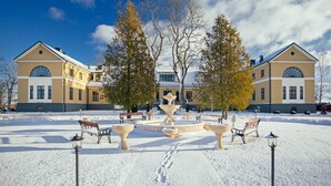 En snötäckt innergård med en fontän, bänkar och en byggnad med välvda fönster.