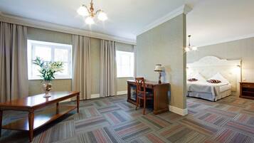 Habitación de hotel con una cama grande, un escritorio con una silla, una mesita con una lámpara y una planta en maceta junto a la ventana.