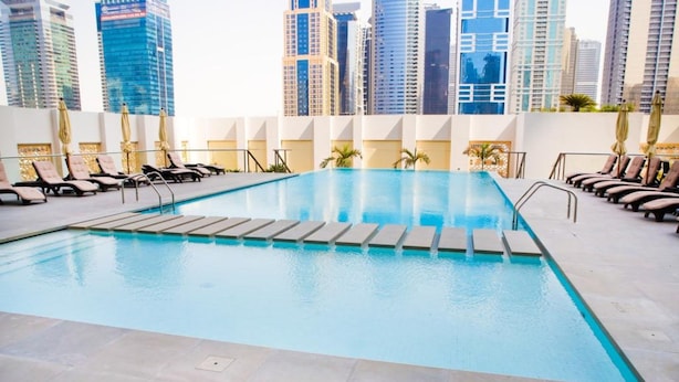 A swimming pool with lounge chairs and umbrellas, surrounded by high-rise buildings. - Piks Key - West Avenue (Dubai)