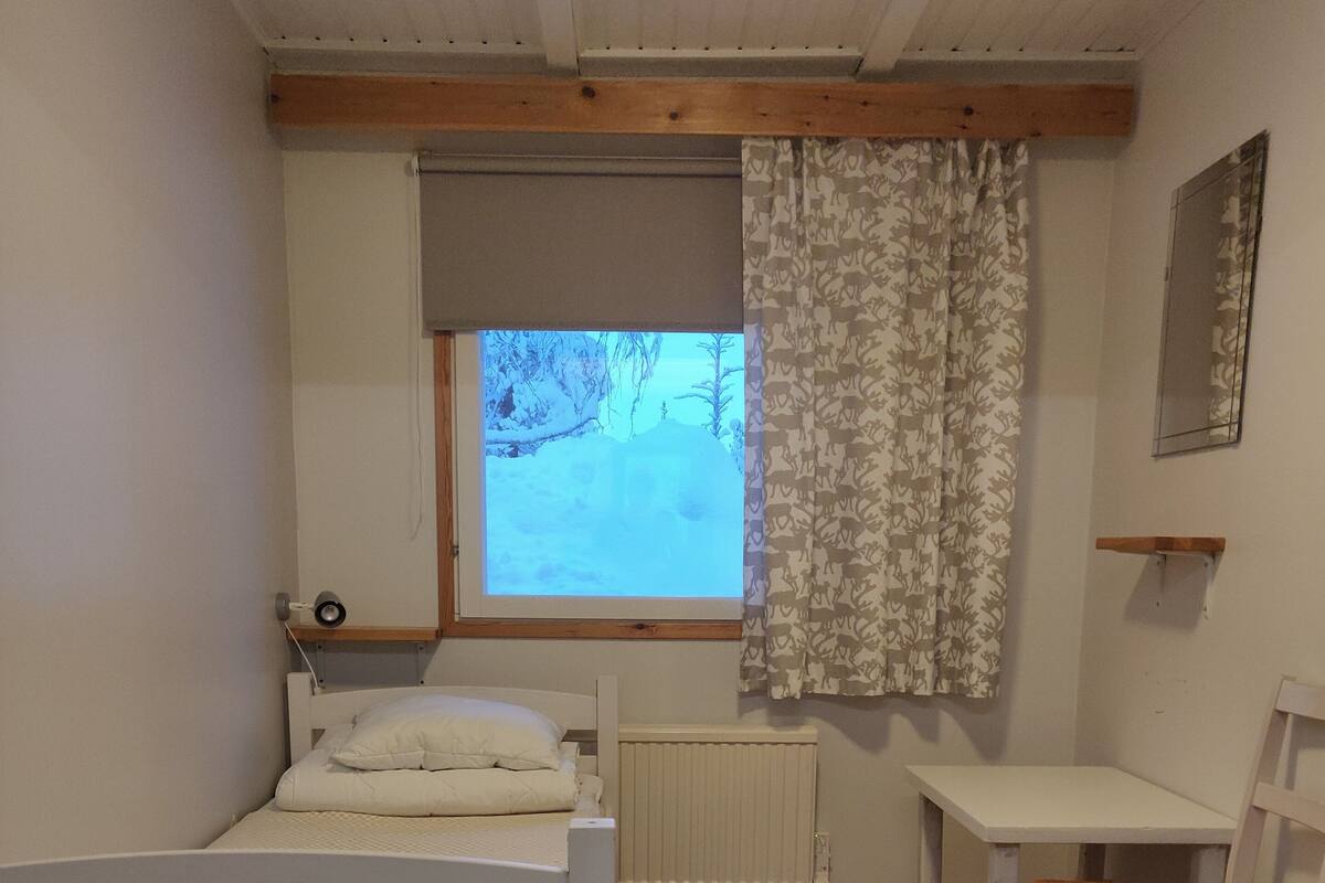 A bedroom with a bed, a window with a view of trees, a radiator, and a small table with a chair.