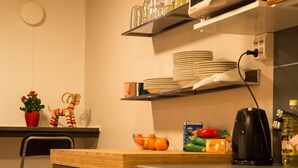 Une cuisine compacte équipée d’un four à micro-ondes, d’étagères pour la vaisselle, d’une bouilloire et de divers ustensiles de cuisine.
