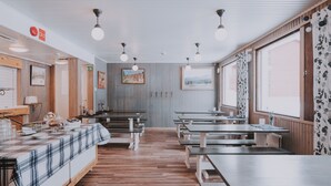 Un restaurant avec des tables et des bancs en bois, un comptoir recouvert d’une nappe à carreaux et des œuvres d’art encadrées accrochées aux murs.
