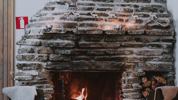 Une cheminée en pierre avec un feu, deux chaises en bois et une petite table placée devant.