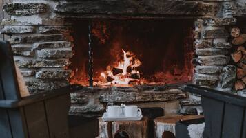 A stone fireplace with a fire burning inside, surrounded by rustic wooden furniture.