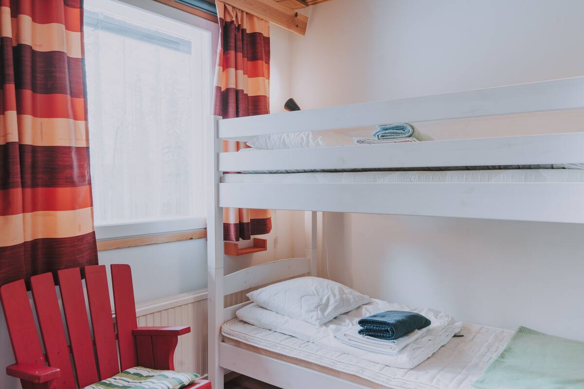 A bunk bed with white bedding and a red chair.