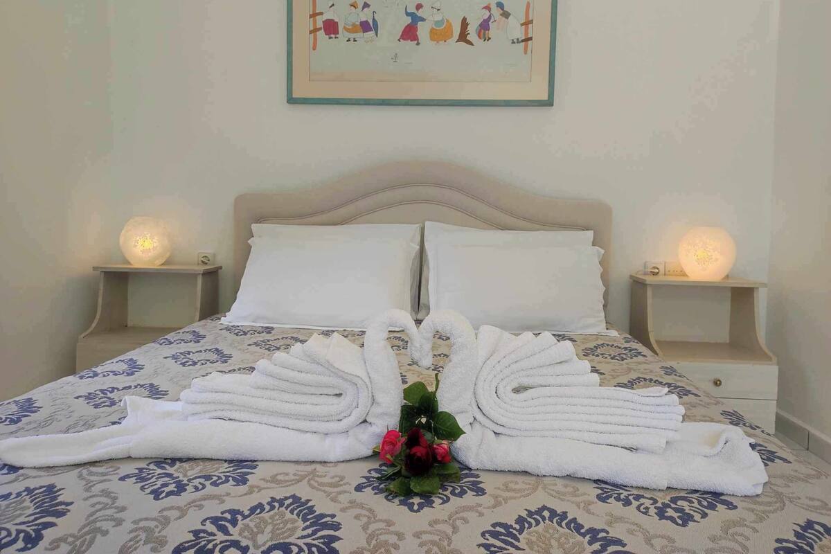 A neatly made bed with white towels arranged in a fan shape, a framed picture on the wall, and bedside lamps.