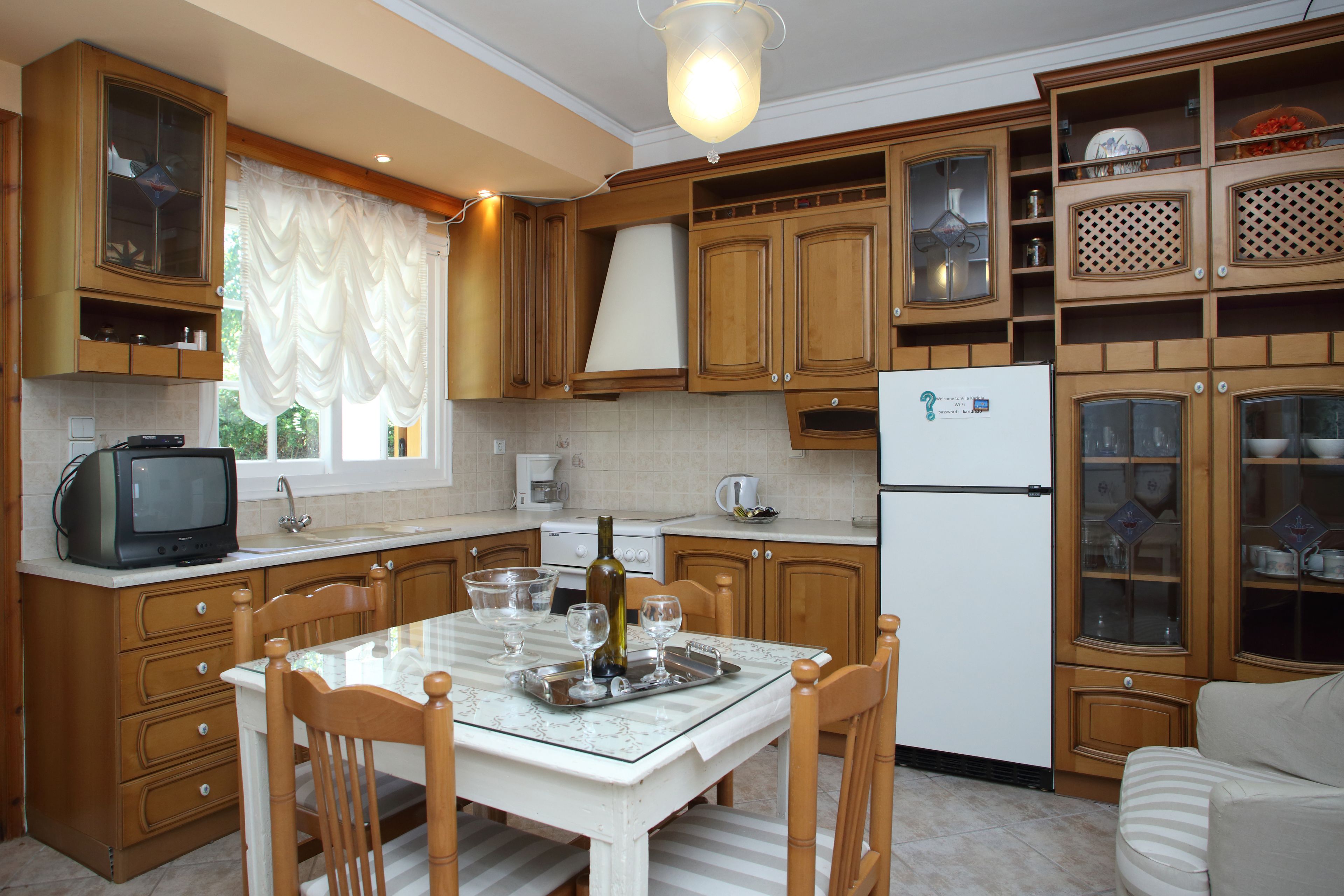 A kitchen with wooden cabinets, a dining table with chairs, a refrigerator, and a television.