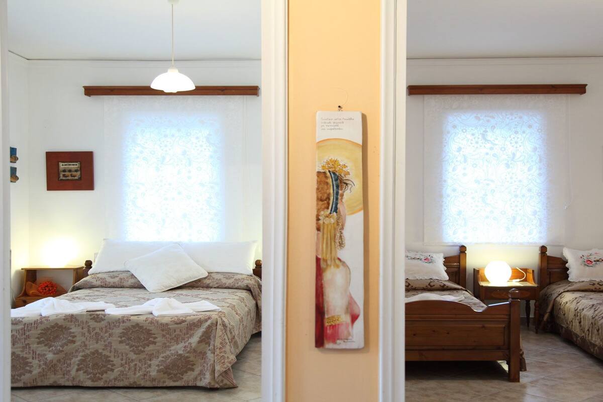 A room with two beds, a wooden headboard, a bedside table with a lamp, and a wall-mounted picture.