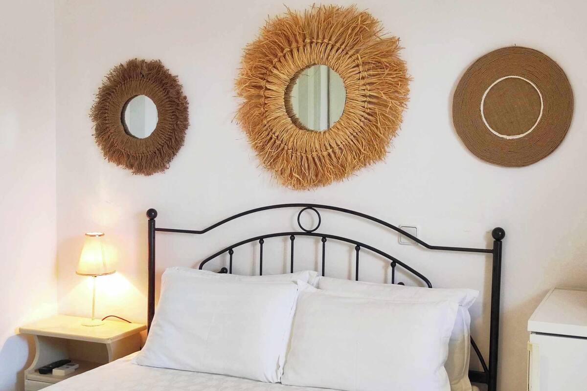A bed with a metal headboard, a nightstand with a lamp, and three woven wall decorations.