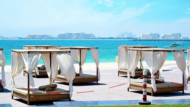 Outdoor beds with white curtains, a beach view, and a distant cityscape. - Piks Key - Bahar 1 (Dubai)