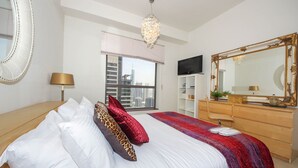 A bedroom with a bed, a dresser, a TV, a large mirror, and a window with a city view. - Piks Key - Bahar 1 (Dubai)