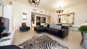 A modern living room with a sectional sofa, a zebra-patterned rug, a large mirror, and a chandelier. - Piks Key - Bahar 1 (Dubai)