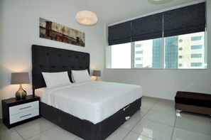 A modern bedroom with a large bed, two bedside tables, a nightstand, a bench, a window with blinds, and a painting on the wall. - Piks Key- Marina Pinnacle (Dubai)