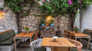 An outdoor seating area with wooden tables and chairs, a stone wall, and potted plants. - Krem Hotel (Cesme)