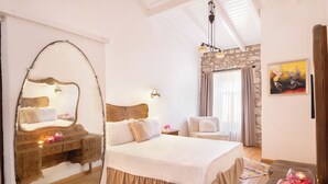 A bedroom with a large bed, a wooden dresser, a mirror, a stone wall, a window with curtains, and a painting on the wall. - Krem Hotel (Cesme)