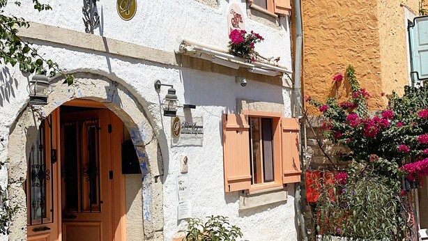 A traditional building with a white facade, wooden shutters, and a stone archway entrance. - Krem Hotel (Cesme)