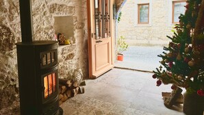 A stone-walled room with a wood-burning stove, a wooden door, and a Christmas tree. - Krem Hotel (Cesme)