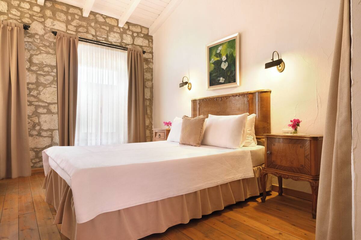 A bedroom with a stone wall, a wooden bed, a nightstand, and a painting on the wall.