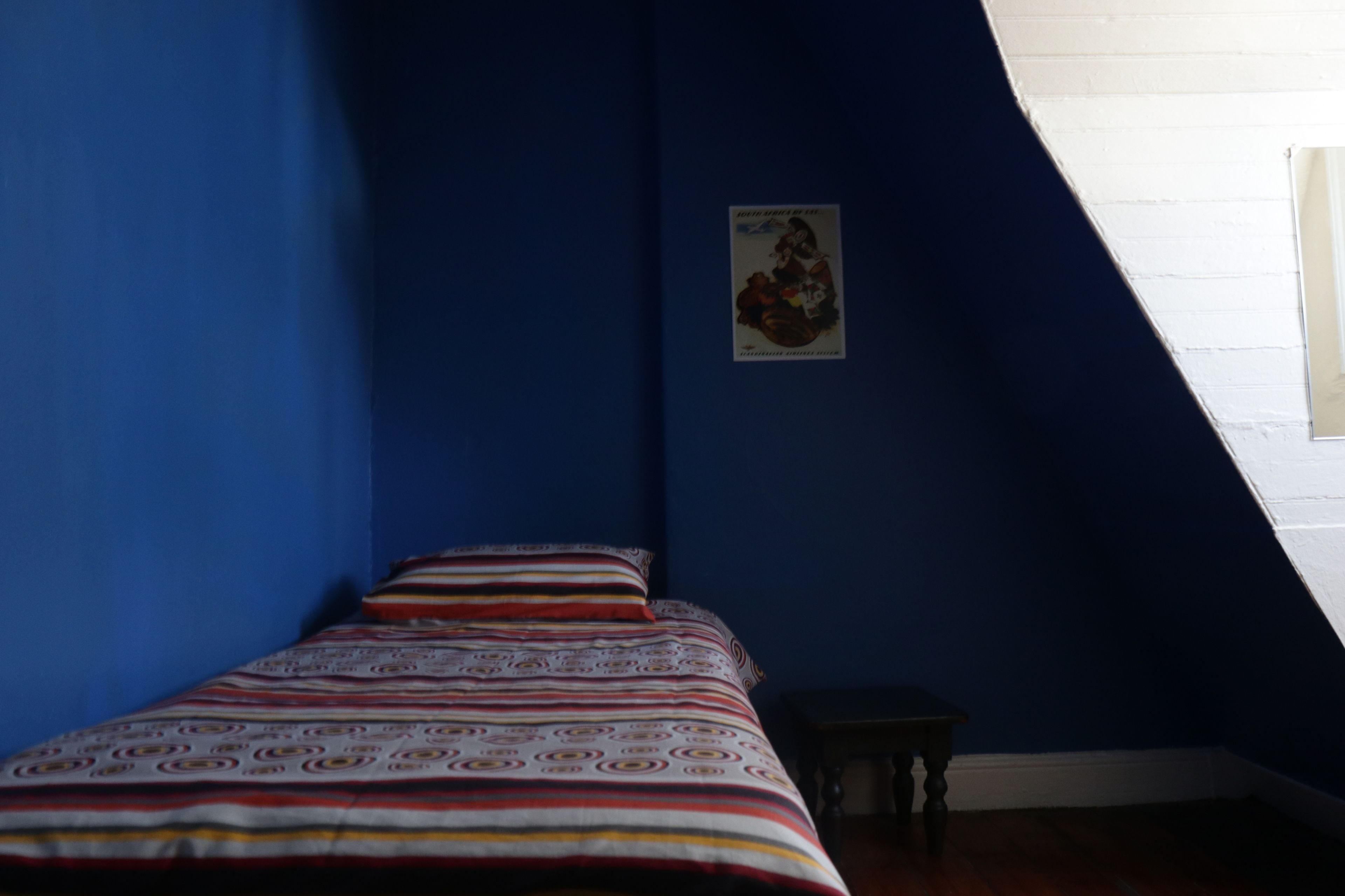Ein Schlafzimmer mit einem Bett an einer blauen Wand, einem kleinen Tisch und einem Bild an der Wand.