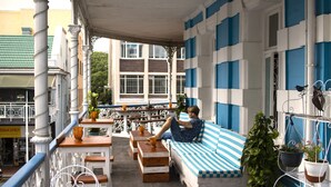 A covered outdoor seating area with a striped blue and white couch, wooden tables, and potted plants. - Urban Hive Backpackers (Cape Town)