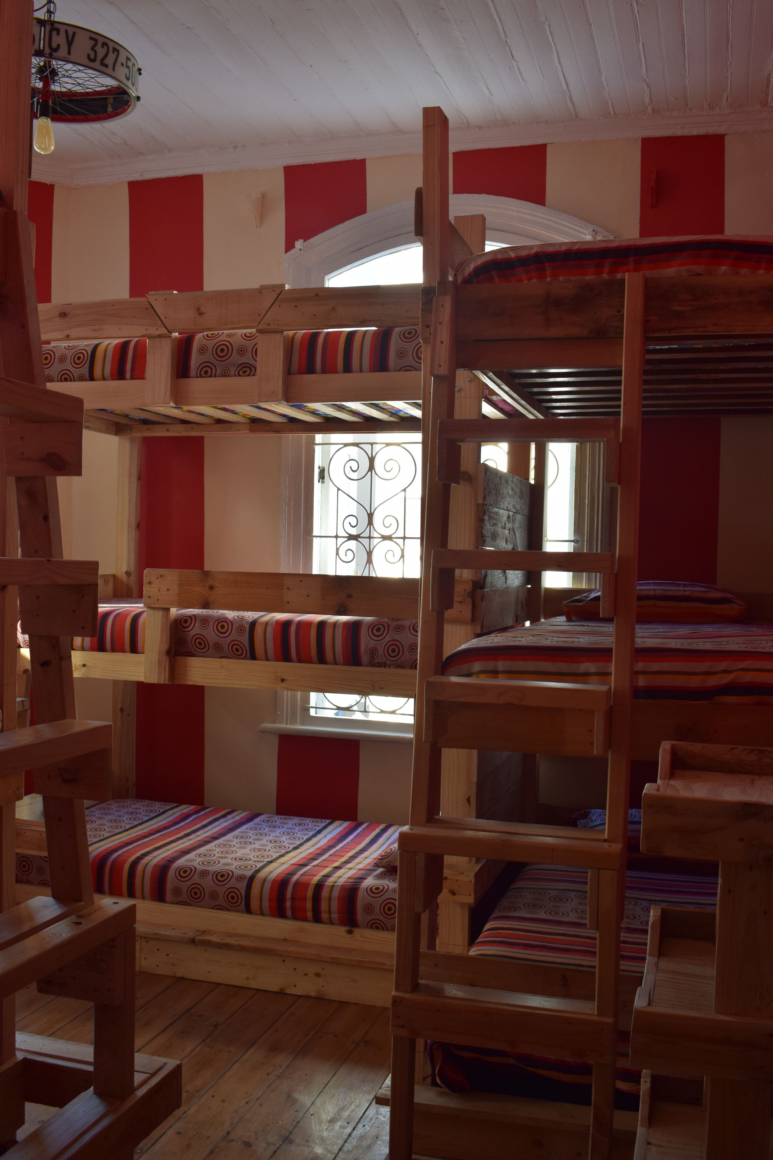 A bunk bed room with a wooden ladder, a window with decorative iron bars, and a red and white striped wall.