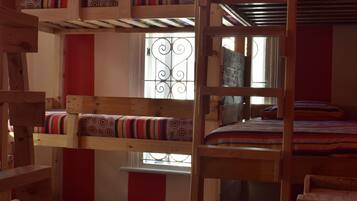 A bunk bed room with a wooden ladder, a window with decorative iron bars, and a red and white striped wall.