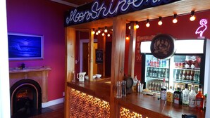 A bar with a neon sign, wooden decor, and a variety of liquor bottles. - Urban Hive Backpackers (Cape Town)