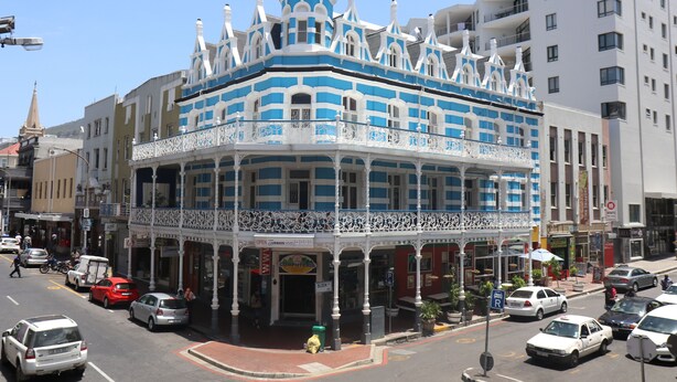 A corner building with a blue and white facade, a balcony, and a sign for a computer store. - Urban Hive Backpackers (Cape Town)