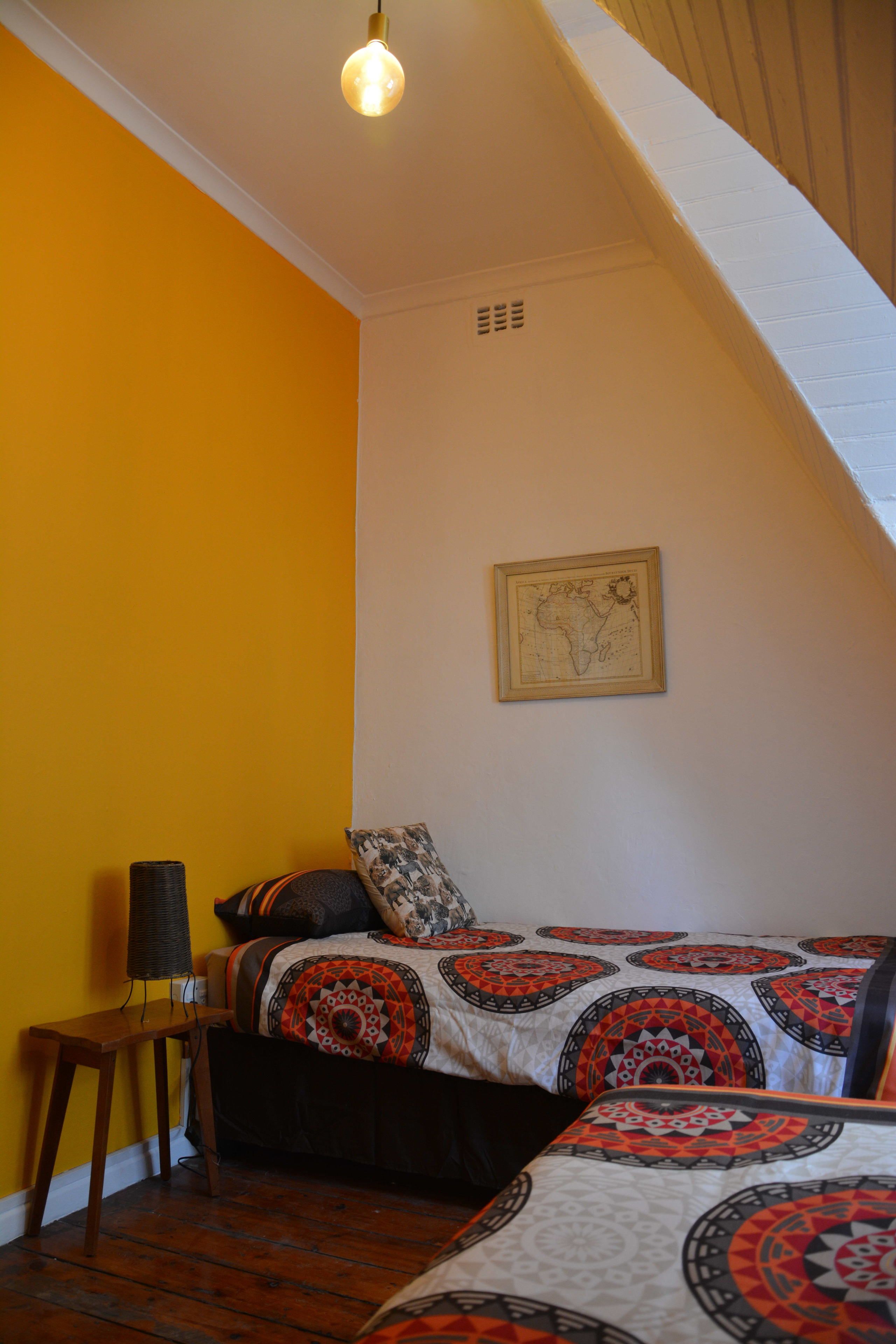 A bedroom with a sloped ceiling, a bed with patterned bedding, a map on the wall, and a lamp on a wooden nightstand.