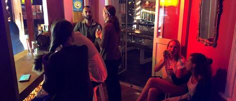 A group of people in a warmly lit indoor setting with a wooden floor and a glass door leading outside.