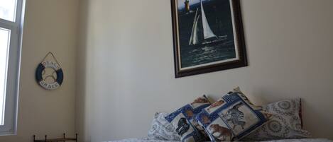 A bedroom with a bed, a framed picture of a sailboat, a wall-mounted sign, and a window.