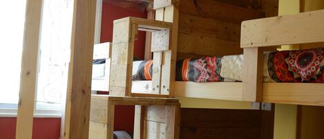 A bunk bed with a wooden frame, a window with a decorative iron grill, and a red wall.