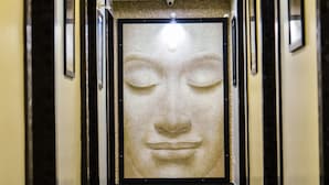Un pasillo con una gran escultura en la pared, cuadros enmarcados y un piso oscuro.