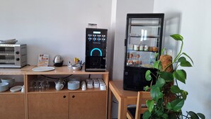 Eine Küchenzeile mit Kaffeemaschine, Kühlschrank und einer Pflanze.