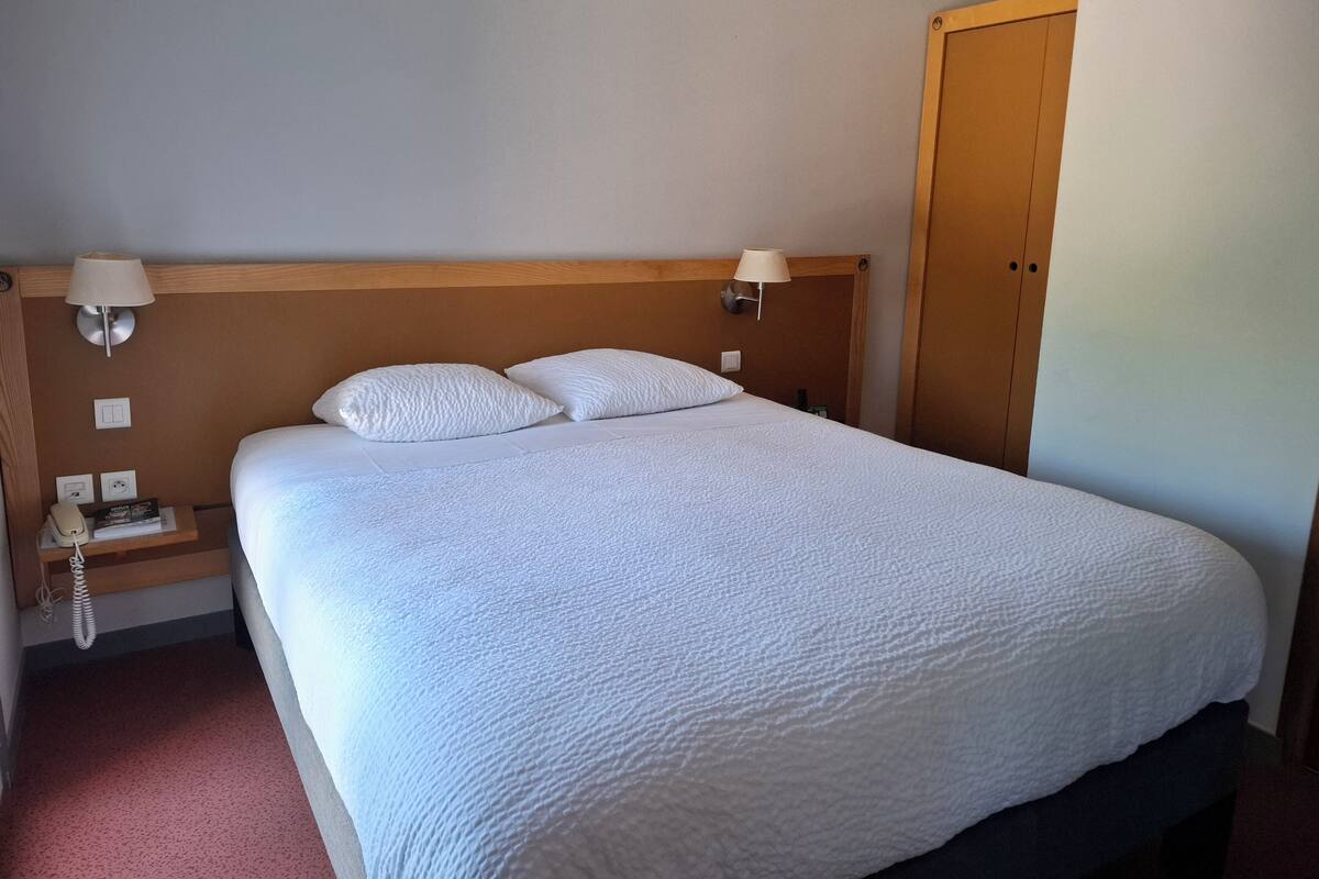 A hotel room with a large bed, two bedside lamps, a telephone, and a wooden wardrobe.