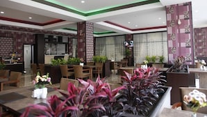 Vestíbulo de hotel con zona de bar, espacios de descanso y plantas decorativas.
