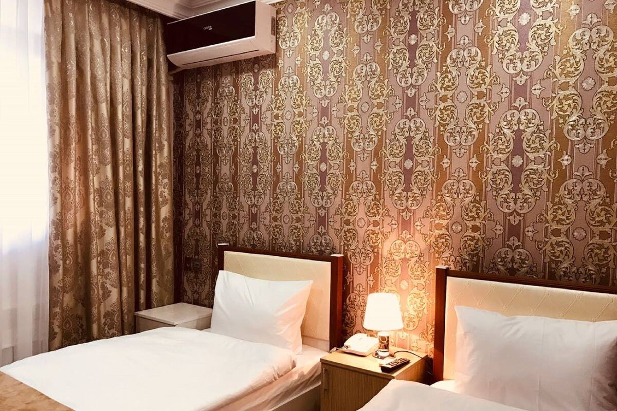 Habitación de hotel con dos camas, una mesita de noche con lámpara y aire acondicionado de pared.