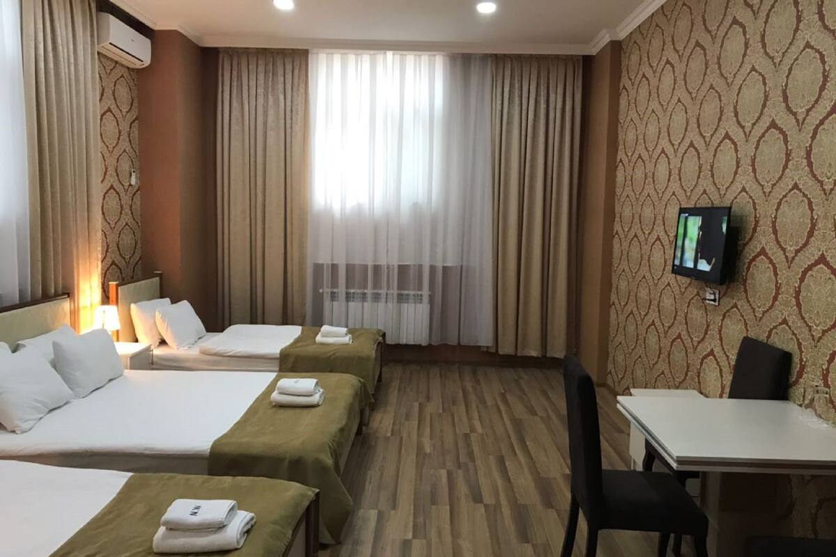 Habitación de hotel con dos camas, un escritorio, una silla, un televisor y una ventana con cortinas.
