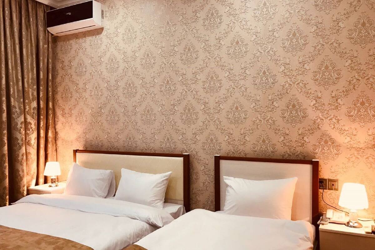 Una habitación de hotel con dos camas, papel tapiz estampado, un equipo de aire acondicionado y lámparas de noche.