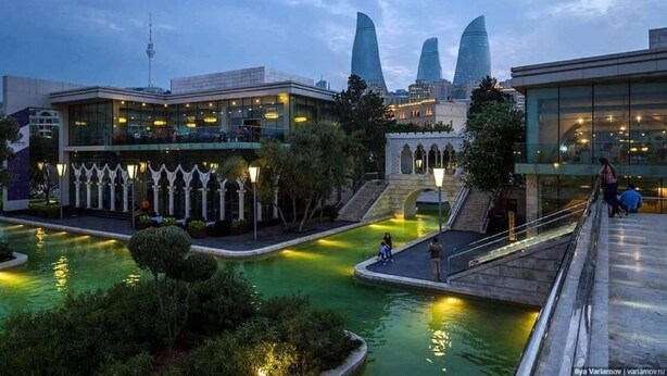 Un edificio moderno con fachada de vidrio, un patio central con fuente de agua y un puente de piedra.