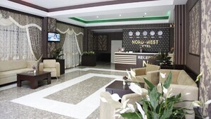 Un vestíbulo de hotel con mostrador de recepción, sofás, una mesa de centro y plantas decorativas.
