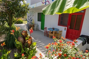 Un patio con zona de comedor, una puerta roja y una ventana verde.