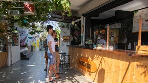 Un comptoir en bois avec une enseigne indiquant « HENDINHEAS » et un tableau affichant le menu. Deux personnes se tiennent devant le comptoir, et on aperçoit une personne à l’intérieur de l’établissement.