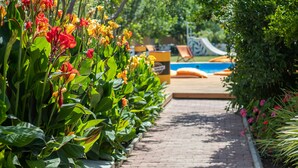Un sentier bordé de fleurs aux couleurs vives qui mène à un espace piscine équipé d’un toboggan.