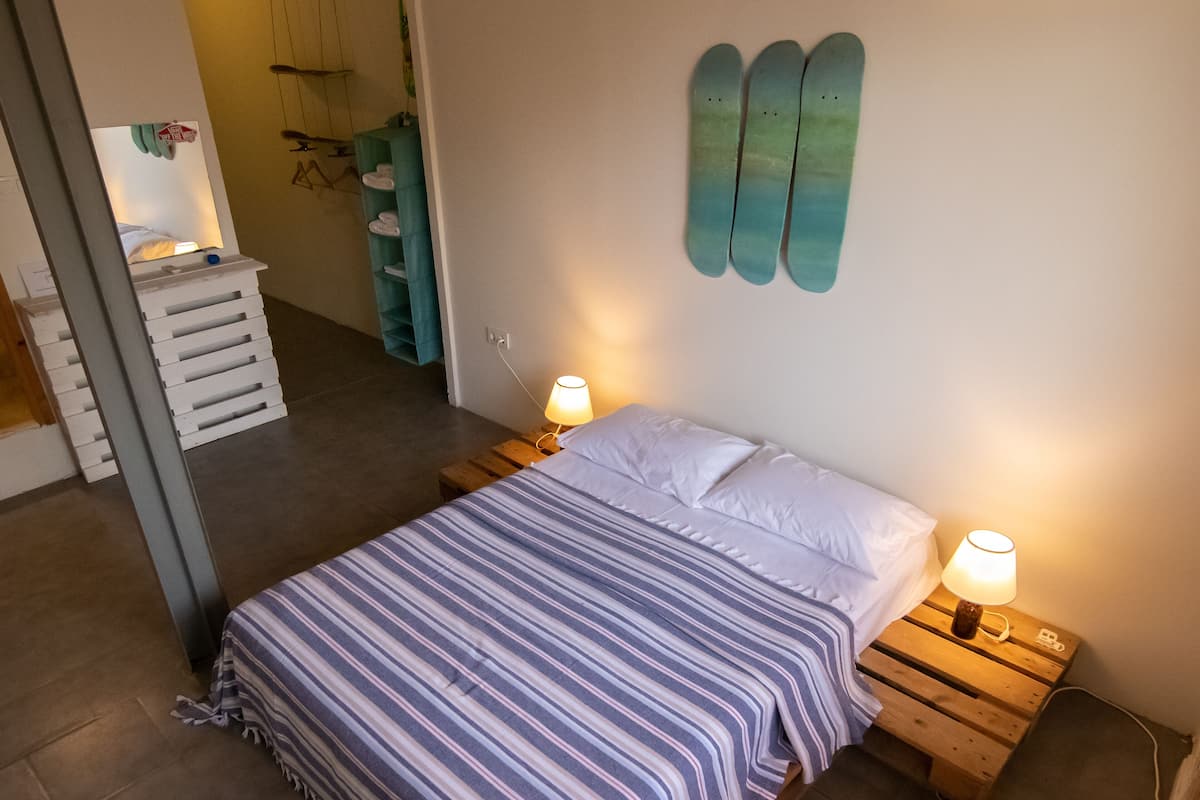 A neatly made bed with striped bedding, two bedside lamps, and a wall-mounted shelf with towels.