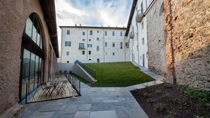 A courtyard with stone flooring, a grassy area, and a building with multiple windows and balconies. - Vistaterra (Parella)